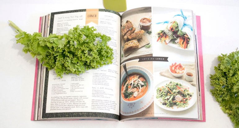 A recipe book opened to show a recipe, a piece of kale covering parts of the left page.